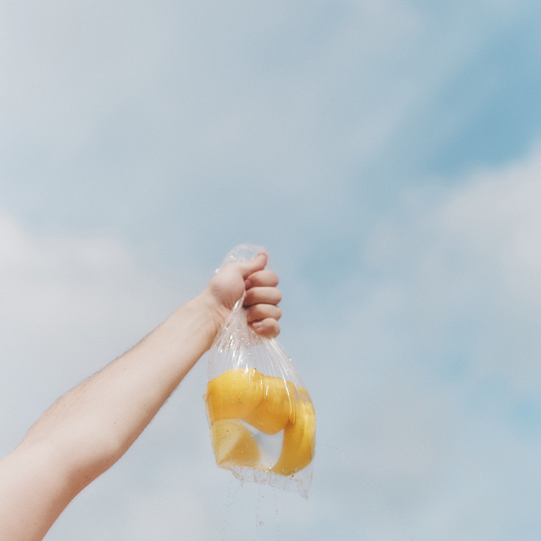 A hand holding a plastic bag filled with lemon slices against a clear blue sky background.